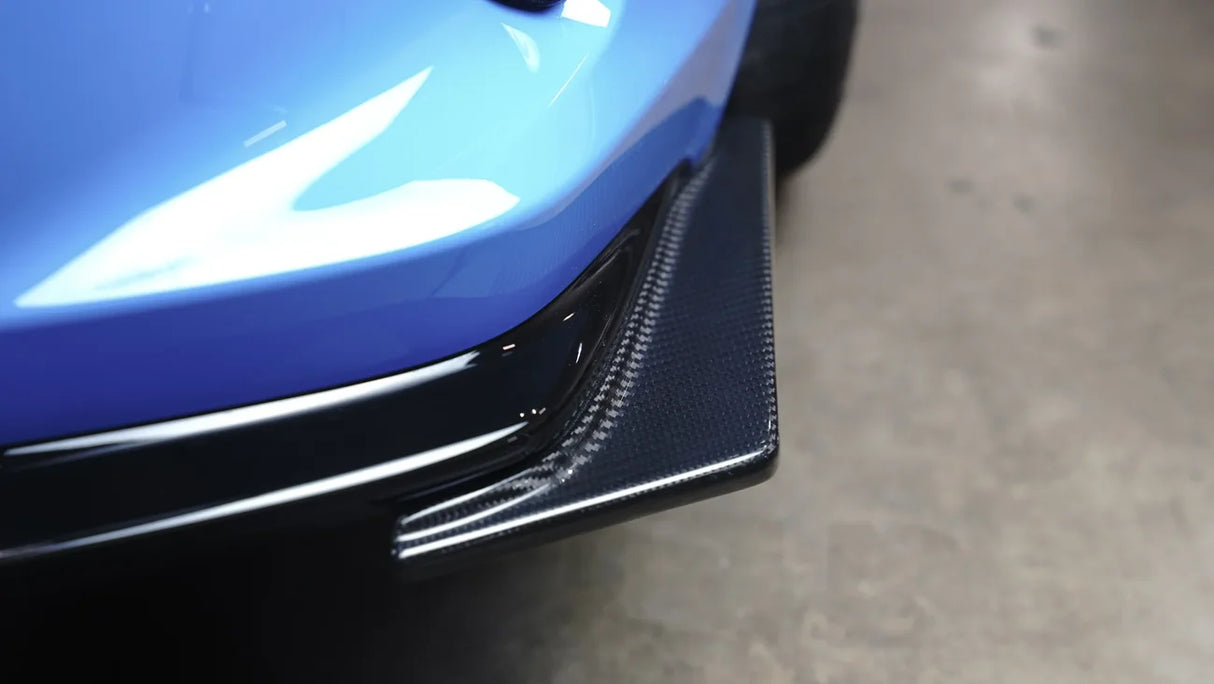 Close-up of a blue car's front bumper with carbon fiber texture.