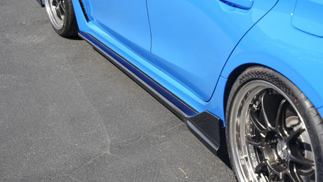 Close-up of a blue car's side with a black rim on a gray pavement.